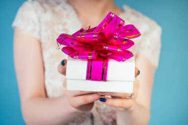 Stüdyoda mavi arka planda pembe kurdeleli, beyaz, şık bir düğün hediyesi kutusu olan gelin..