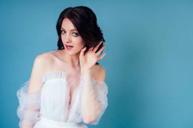 Gelinlik giymiş Hintli bir kadın stüdyodaki mavi arka planda kulak misafiri oluyor ve dedikodu yapıyor.