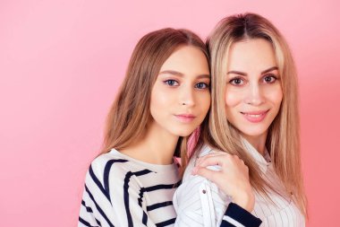 Güzel ve güzel bir genç kız stüdyoda sevgili annesine pembe bir arka planda sarılıyor. Aile refahı ve anneler günü kavramı