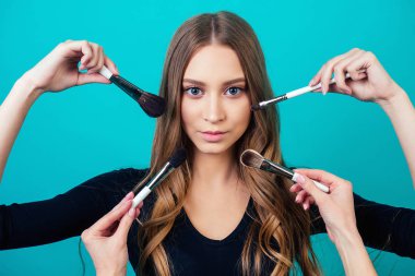 Makyajlı ve saç stili olan genç ve güzel bir kadın vizörlü portresi stüdyonun mavi arka planında bir sürü el ve fırça kullanılıyor.