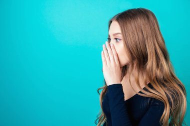 Sarışın ve makyajlı genç ve çekici bir kadının portresi stüdyoda mavi arka planda gizli bir gizemi fısıldıyor. Dedikodu ve gizlilik kavramı