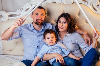 happy family handsome man and charming woman and their cute little son together make the roof on bed in bedroom . concept of buying a cozy and warm house apartment by young family