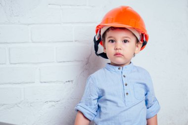 Fırça fırçası tutan genç müteahhit miğferli şirin bir çocuk boyalı beyaz boyalı bir duvar. Ev onarımı konsepti