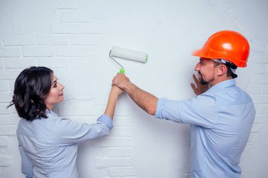 İnşaat kaskı takan mutlu aile yakışıklısı adam ve büyüleyici kadın birlikte beyaz tuğla duvar boyuyorlar. Yeni evliler için rahat ve sıcak bir daire alma fikri