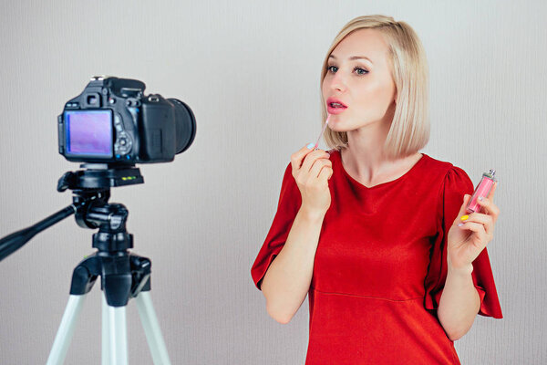 attractive blond videoblogger beauty blogger woman in a red dress records video blog about the care of the skin of the face and cosmetics on a video camera . concept of online makeup courses