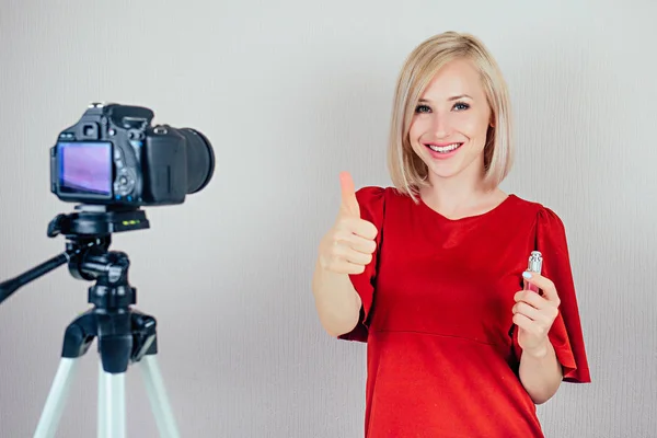 attractive blond videoblogger beauty blogger woman in a red dress records video blog about the care of the skin of the face and cosmetics on a video camera . concept of online makeup courses