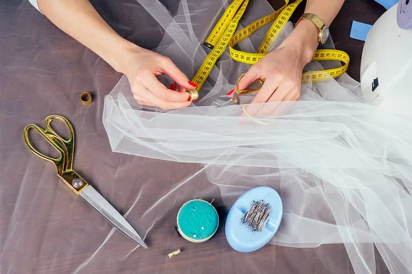 closeup woman hands tailor wedding dressmaker seamstress sew on the sewing machine on a blue background in the studio. The concept of creating a new collection of wedding dress