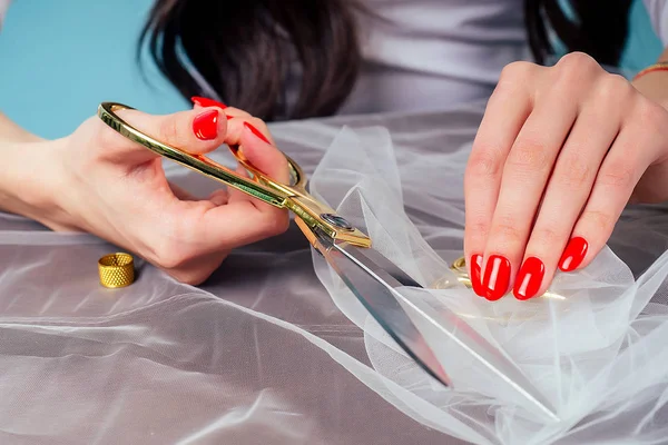 Costureira costureira costureira mulheres mãos com manicure vermelho segura tesoura e corta tecido na mesa no estúdio . — Fotografia de Stock