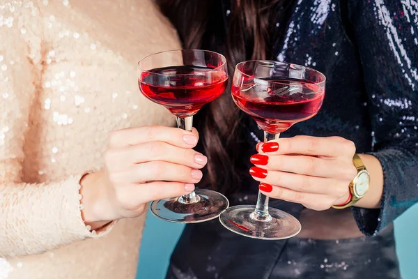 Mani di due donne in abito sera cocktail lucido paillettes stanno tenendo un bicchiere di vino ad una festa in studio sfondo blu — Foto Stock