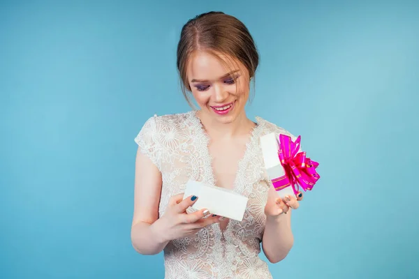 Attraktives Lächeln überraschte schöne Frau Braut mit Make-up in chic sexy weißen Hochzeit hält Geschenkbox im Studio auf blauem Hintergrund. Konzept des Shoppings für eine Hochzeitsgesellschaft — Stockfoto