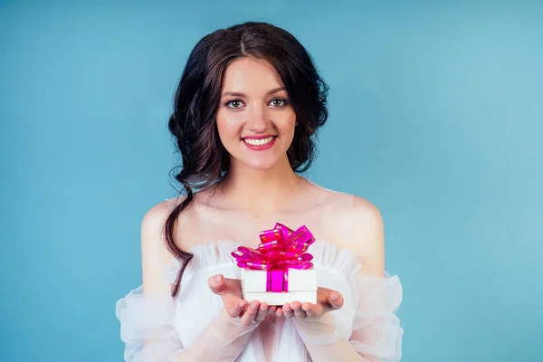 Attraktives Lächeln überraschte schöne Frau Braut mit Make-up in chic sexy weißen Hochzeit hält Geschenkbox im Studio auf blauem Hintergrund. Konzept der Geburtstags- und Hochzeitsfeier — Stockfoto