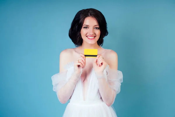 Die Braut im Brautkleid hält eine Kreditkarte in der Hand auf blauem Hintergrund im Atelier — Stockfoto