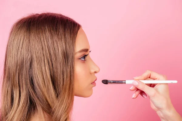 Retrato de chica joven y atractiva y artista de maquillaje visagista aplica lápiz labial de maquillaje a los labios en el estudio sobre un fondo rosa. concepto de maquillaje cuidado de la piel y la belleza — Foto de Stock