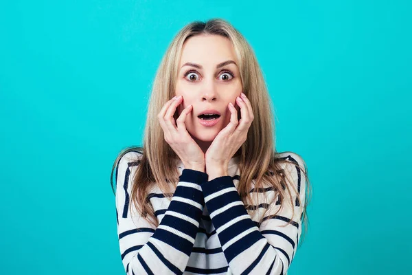 Ritratto di una giovane attraente donna scioccata con i capelli biondi e la bocca di trucco aperta di sorpresa in studio su uno sfondo blu. il concetto di stupito e wow news — Foto Stock