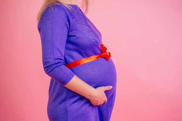 Close-up hands belly baby bump of a pregnant woman hug in a dress in studio on a pink background . concept of love for the baby — 图库照片