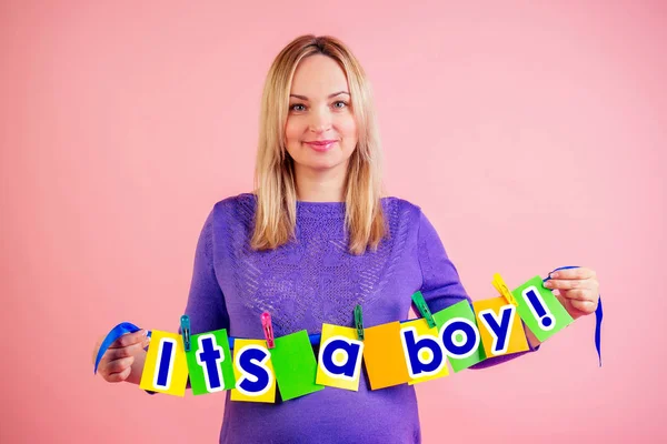 Beautiful pregnant big belly woman hold a cards with the inscription its a boy in studio on pink background . waiting for childbirth — Stok fotoğraf