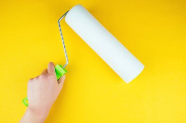 Sarı arka planda boya silindirli el.