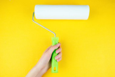 Sarı arka planda boya silindirli el.