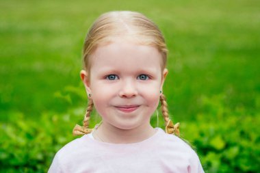 Şirin gri elbiseli tatlı sarışın kız. Parkta ağaçların ve yeşilliklerin arkasında güzel bir gülümseme.