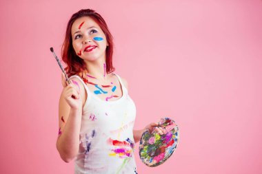 Eğlenceli, kirli makyaj sanatçısı. Stüdyoda pembe bir arka planda, yüz paletinde boya lekesi var.