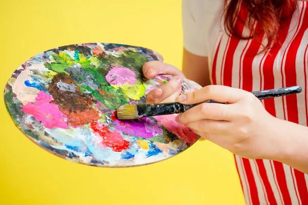 Primo piano di mani di pittore d'artista in una tavolozza di grembiule, tubo di vernice, spazzole su uno sfondo rosa in studio. musa e ispirazione idea — Foto Stock