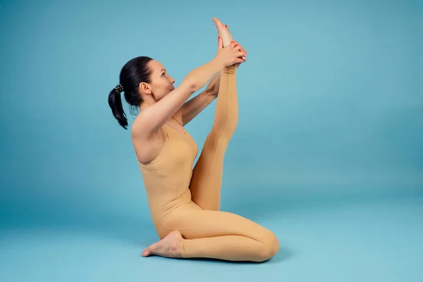 Retrato de uma bela e jovem mulher de ioga fazendo aquecimento e alongamento acrobacias elementos no chão em um fundo azul no estúdio — Fotografia de Stock