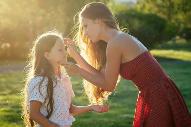 İlgili ve uzun saçlı, kokteyl kırmızısı elbiseli güzel bir anne yazın parkta kızlarının yüzünü ıslak peçetelerle siler. Antibakteriyel peçeteler ve tazelik kavramı