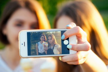 İki güzel kız arkadaş liseli kız parkta telefonda selfie çekiyor.