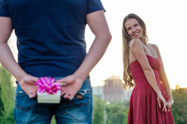 迷人迷人的金发美女穿着晚礼服恋爱中的妻子，在夏日公园里等待着恋人的礼品盒，她的背景是草绿色的。 结婚周年的概念 — 图库照片