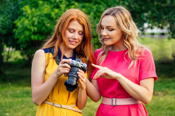 Fotosessão bela jovem ruiva irlandesa menina em um vestido amarelo e mulher loira europeia em vestido rosa fotografados uns aos outros no parque de verão. fotocaça de duas namoradas modelo — Fotografia de Stock