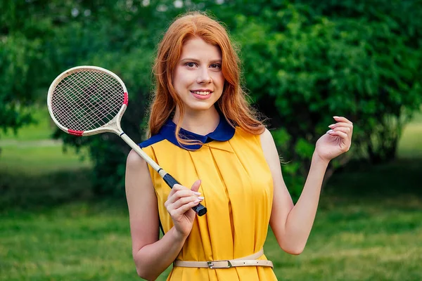 Aktif ceria cantik ginger berambut merah muda Irlandia wanita norwegian dalam gaun kuning dan dalam merah muda bermain raket bulu tangkis tenis di taman musim panas — Stok Foto