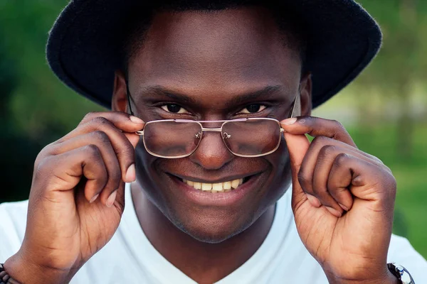 portrait of black men in stylish suits and black hat with glasses in a summer park. African-Americans handsome model hispanic businessman fresh snow-white smile . dentist and teeth whitening concept