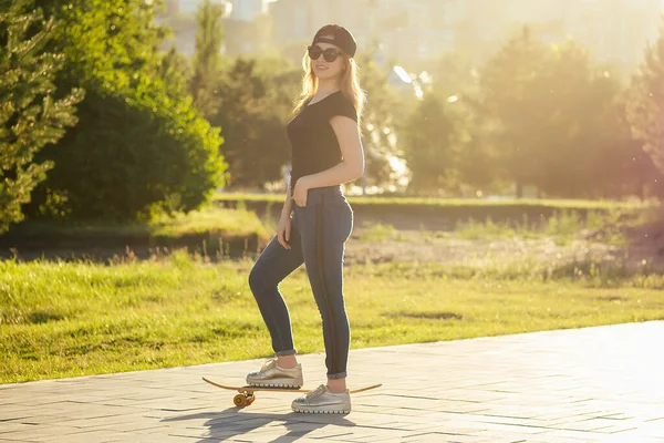 Flickåkare i en sommarpark. ben fötter kvinna i fashionabla jeans och snygga sneakers på en skateboard longboard footway asfalt. Begreppet skateboard för ungdomsverksamhet — Stockfoto