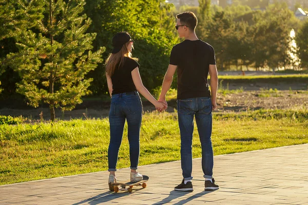 Aktív pár a szerelem sport korcsolyázás a nyári parkban. gyönyörű nő és férfi szórakozni gördeszka longboard háttér a folyó. Férfi és lány randi. aktív életmód a fiatalok körében — Stock Fotó