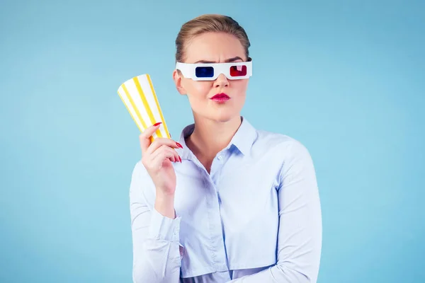 Несчастная недовольная женщина смотрит 3D фильм в очках с чашей с попкорном на синем фоне в изолированной студии — стоковое фото
