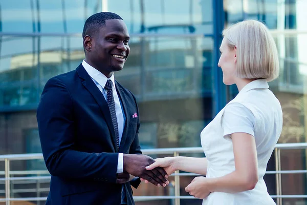 Stilig afroamerikansk man i svart kostym skakar hand med en affärskvinna partner stadsbild glas kontor bakgrund. lagarbete och lyckad affärsidé — Stockfoto