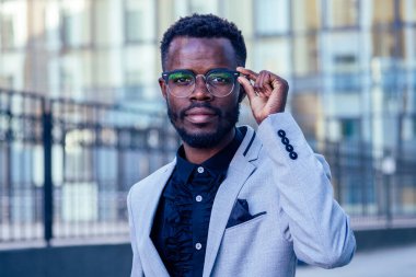 şık ceketli ve beyaz yakalı beyaz gömlekli yakışıklı ve şık Afro-Amerikan işadamı Manhattan cam ofislerinin arka planında