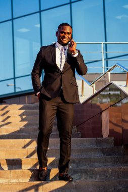 Yakışıklı ve şık afro-amerikan iş adamı şık siyah ceketli ve yakalı beyaz gömlekli Manhattan cam ofis manzaralı