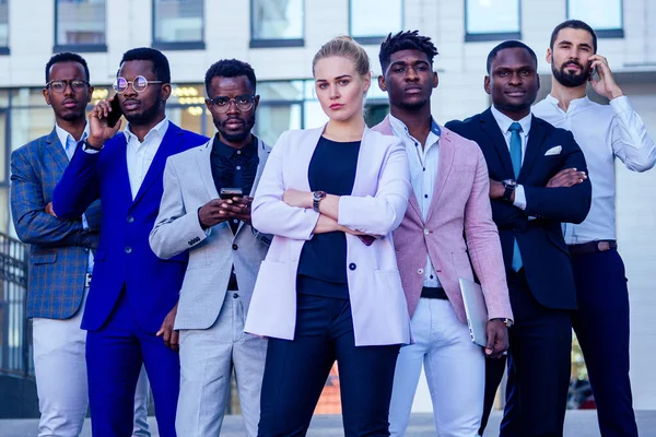 En grupp om sju framgångsrika affärsmän affärsslady och hennes manliga partners i snygga kostymer står och tittar stolt utomhus. lagarbete och begreppet multietniskt företag — Stockfoto