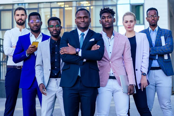 Un grupo de siete hombres y mujeres de negocios de éxito en trajes elegantes de pie y buscando orgullosamente al aire libre. el trabajo en equipo y el concepto de empresa multiétnica —  Fotos de Stock