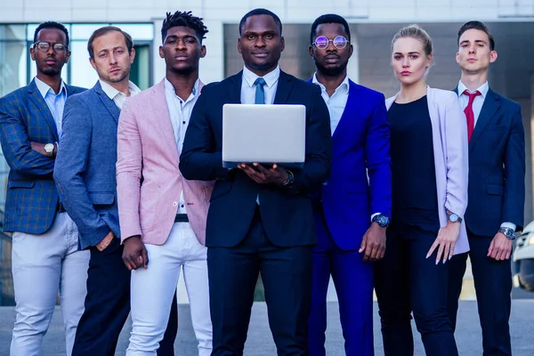 Um grupo de sete empresários de sucesso homens e mulheres em ternos elegantes de pé e olhando orgulhosamente ao ar livre. o trabalho em equipa e o conceito de empresa multiétnica — Fotografia de Stock