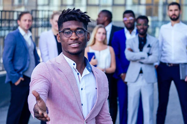 Homem afro-americano bem sucedido e bonito em um terno de negócios elegante dando uma mão para um sinal de aperto de mão bem-vindo à frente de um grupo um monte de pessoas multirracial empresa multiétnica — Fotografia de Stock