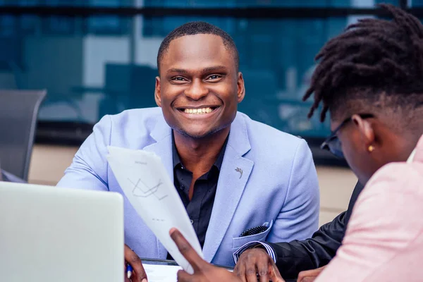 Dos elegantes empresarios afroamericanos se asocian con empresarios en trajes de negocios de moda sentados a la mesa en un café de verano al aire libre —  Fotos de Stock