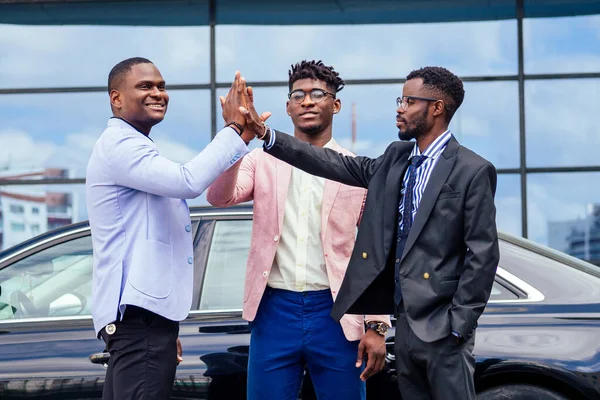 Um grupo de seus três empresários afro-americanos de sucesso em um terno elegante conversando e se alegrando no fundo da janela do arranha-céu de rua. trabalho em equipe e conceito de sucesso — Fotografia de Stock