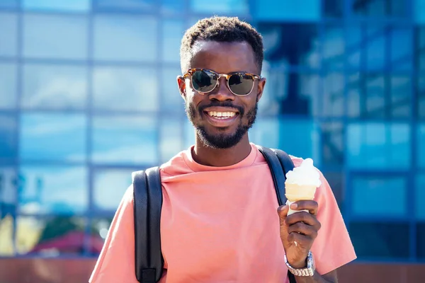 Cara afro-americano fresco e elegante em óculos de sol comendo sorvete em um chifre de waffle no verão no parque — Fotografia de Stock