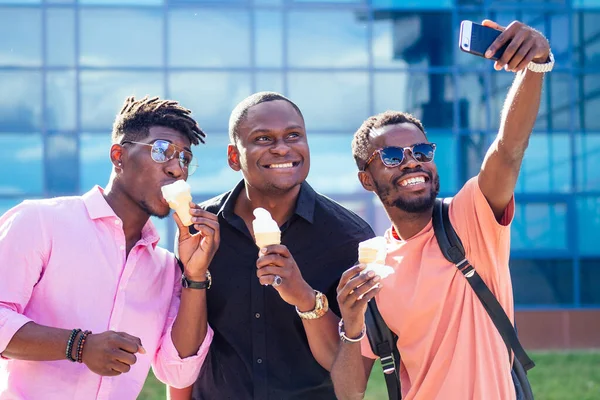 En grupp om tre afroamerikanska killen äter glass i ett våffelhorn på sommaren i parken — Stockfoto