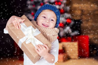 Beyaz tişörtlü, mavi şapkalı, elinde yeni yıl hediyesi olan küçük mutlu sarışın çocuğun elinde şömine ve yılbaşı ağacı olan bulanık bir Noel stüdyosu. Noel arifesi sihirli büyüsü.