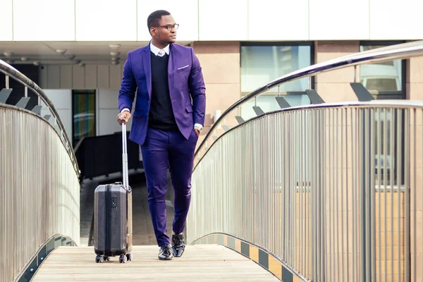 Retrato de cuerpo completo del hombre viajero guapo afroamericano bien vestido elegante hombre de negocios caminando con la maleta saliendo de la llegada del aeropuerto a casa después de la reunión de negocios — Foto de Stock