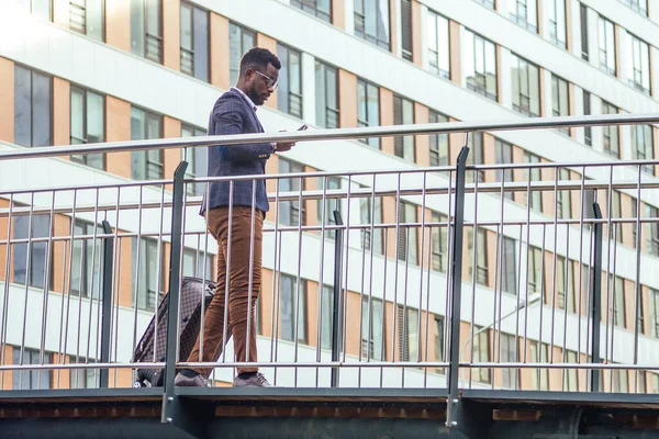 Full längd porträtt av framgångsrika och välklädda afroamerikanska affärsman promenader för flygning på flygplatsen med hjulväska stor resväska på hjul — Stockfoto