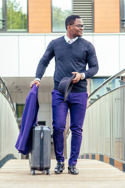 Full body portrait of handsome traveler man African american well dressed stylish businessman walking with suitcase leaving the airport arrival home after business meeting